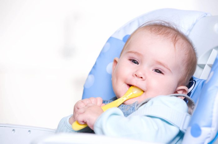 Beautiful happy baby with spoon sitting on highchair