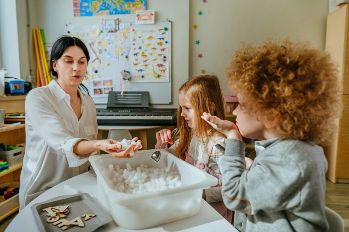 Learning play activities in kindergarten or daycare centre. Preschool students looking for letter forms in a container with styrofoam. Education concept. Selective focus.