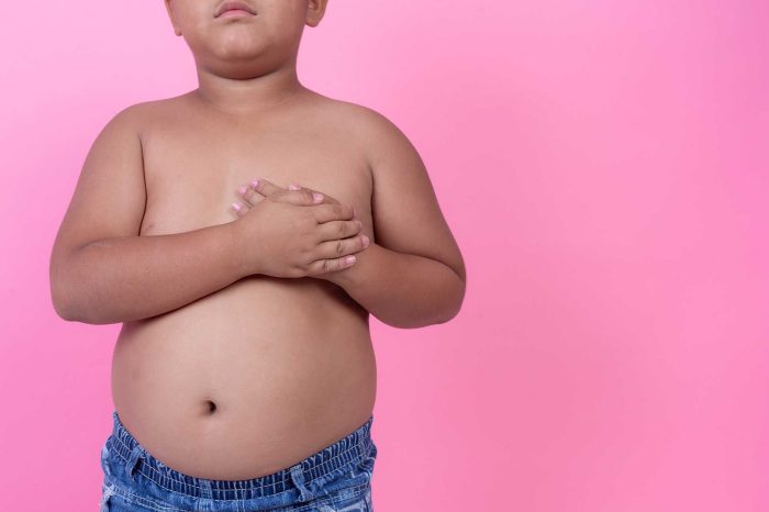 Obese boy who is overweight on a pink background.
