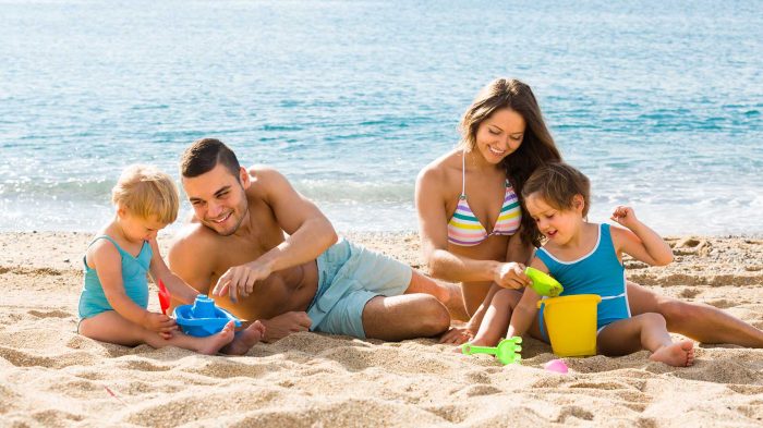 Happy smiling family of four playing with sand at beach in sunny day